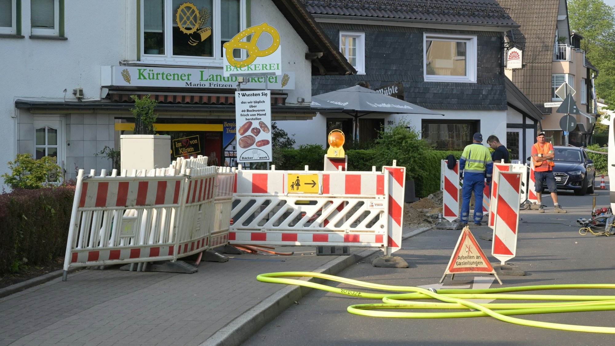 Warnbaken stehen auf einer Straße und dem angrenzenden Bürgersteig vor einer Bäckerei.