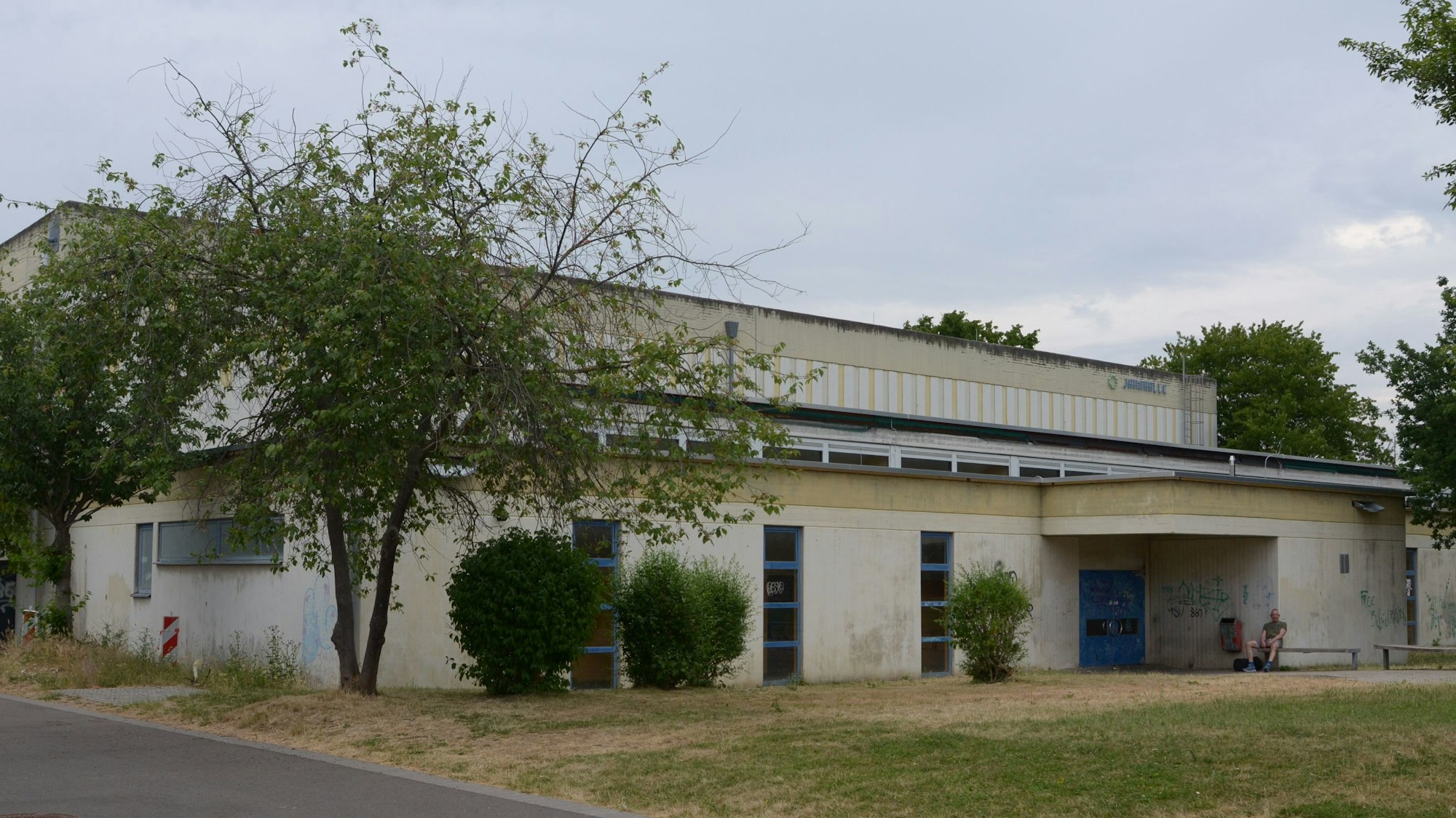 Das Bild zeigt die von Bäumen und Sträuchern umgebene Sporthalle.