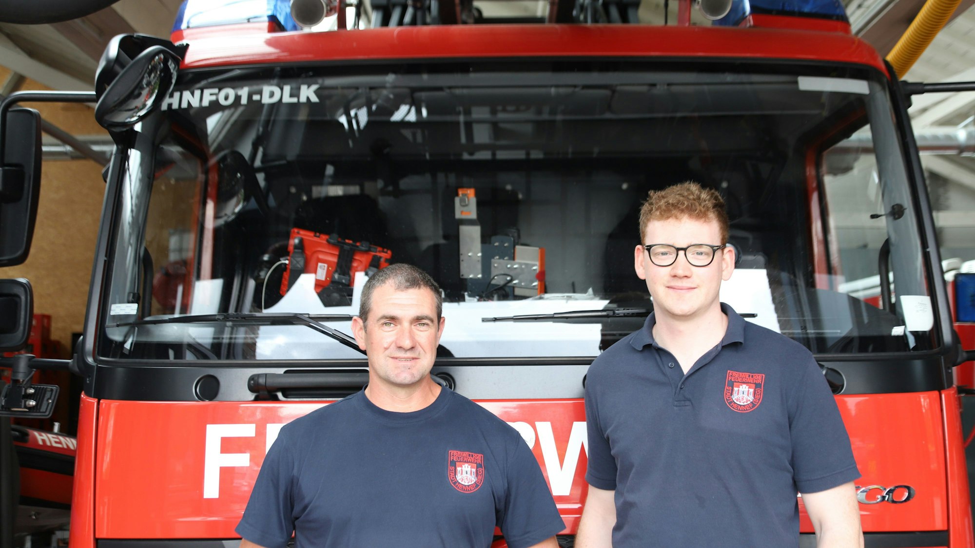 Zwei Männer in T-Shirts der Hennefer Feuerwehr stehen vor einem Löschfahrzeug.
