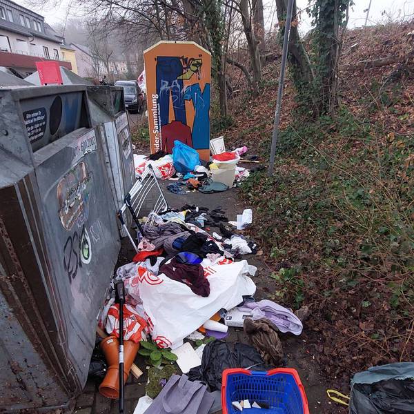 Allerlei Müll liegt vor einem Container auf der Erde.