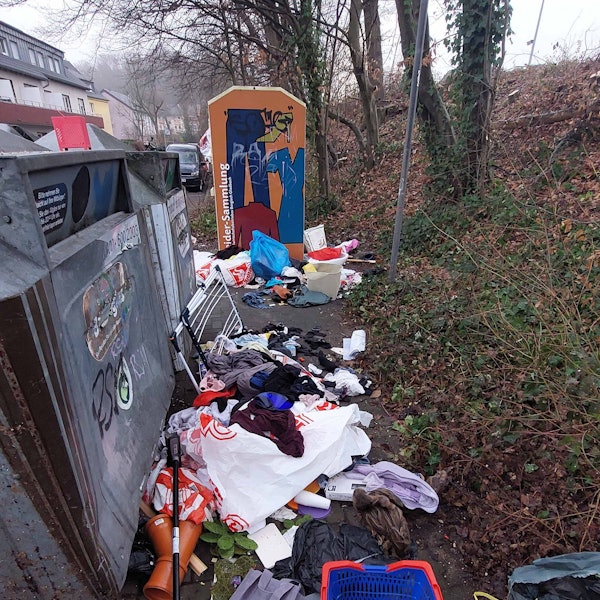 Allerlei Müll liegt vor einem Container auf der Erde.