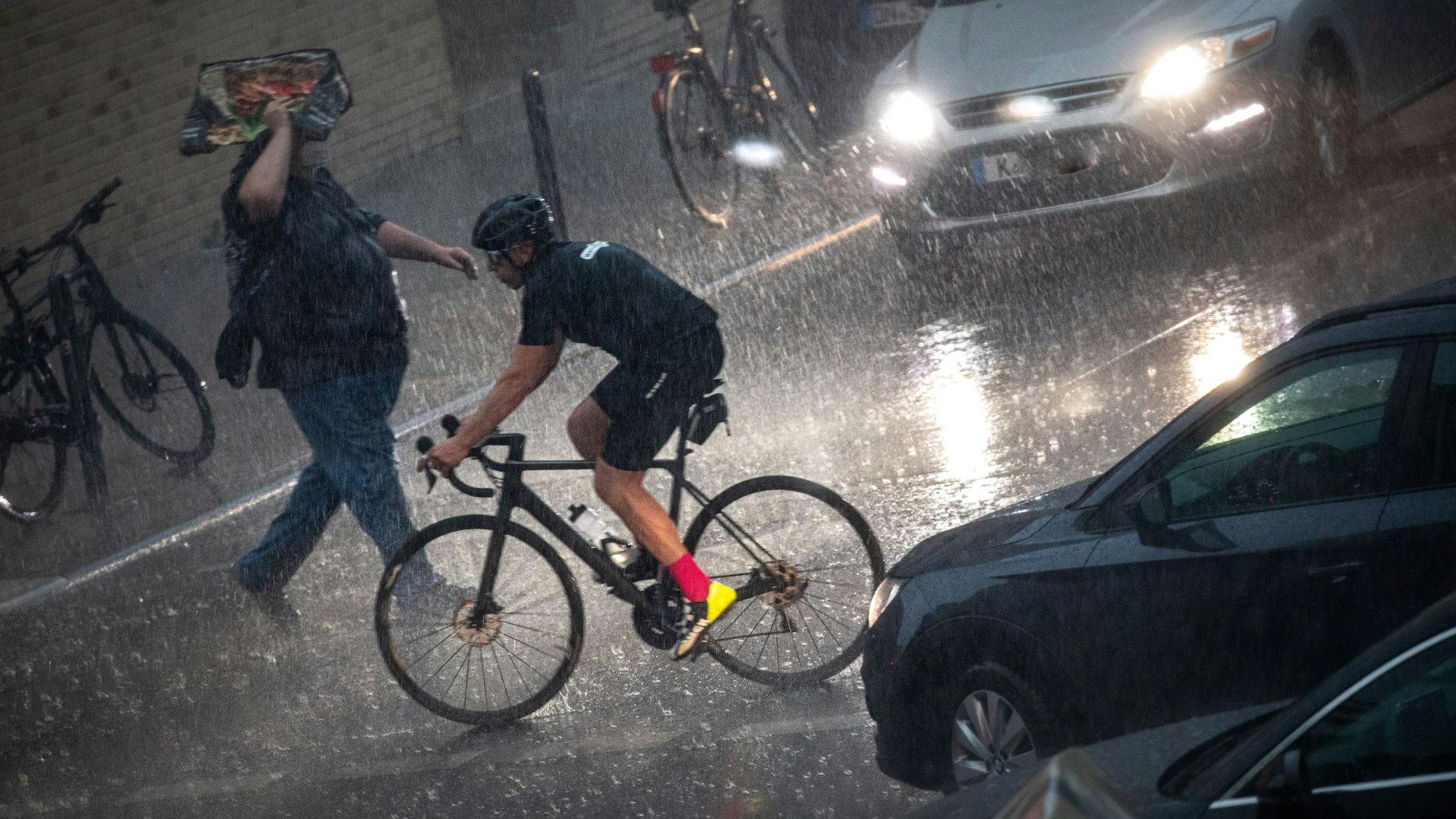19.05.2022, Köln: Ein Rennradfahrer sitzt auf seinem Rennrad und eine Person geht über die Straße während eines Unwetters mit Gewitter und Starkregen im Ortsteil Sülz über die Straße. Foto: Matthias Heinekamp