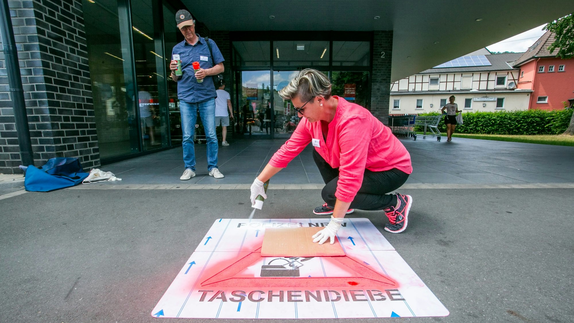 Eine Frau Sprühfarbe auf eine Schablone in Form eines Warndreiecks, deren Schriftzug „Polizei NRW – Taschendiebe“ lautet.