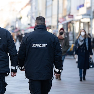 Mitarbeiter vom Ordnungsamt laufen durch eine Fußgängerzone. Sie sind von hinten zu sehen.