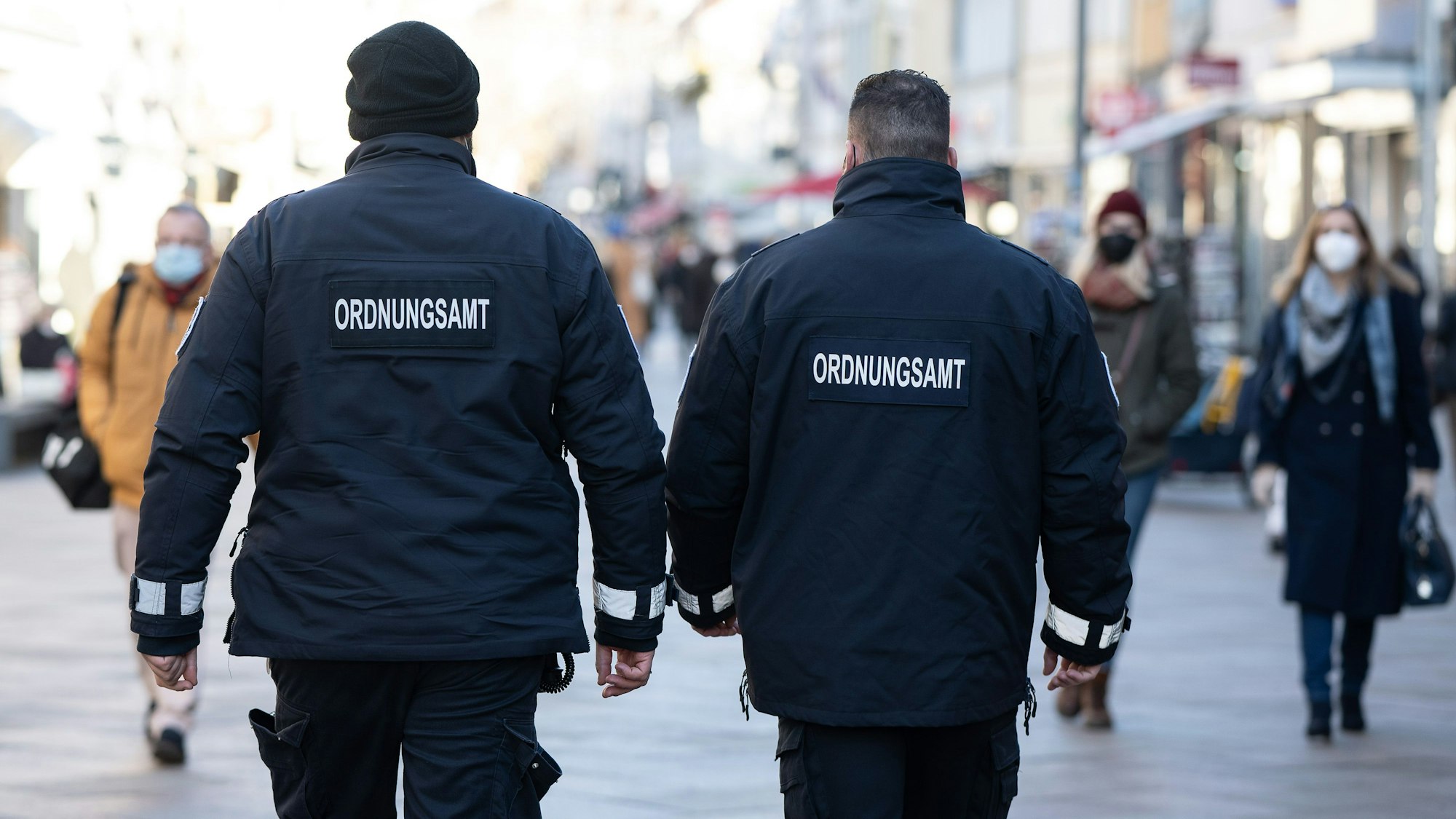 Mitarbeiter vom Ordnungsamt laufen durch eine Fußgängerzone. Sie sind von hinten zu sehen.