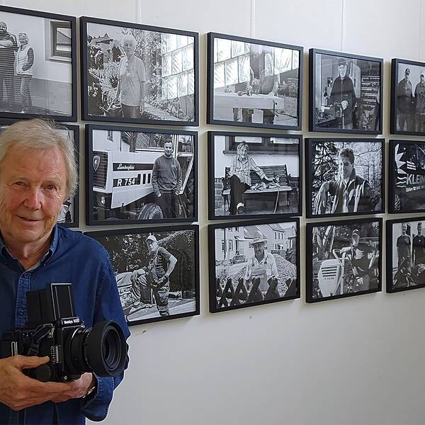 Der Fotograf Dietrich Schubert steht mit seiner Kamara vor einigen seiner Fotos.