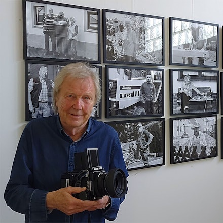 Der Fotograf Dietrich Schubert steht mit seiner Kamara vor einigen seiner Fotos.