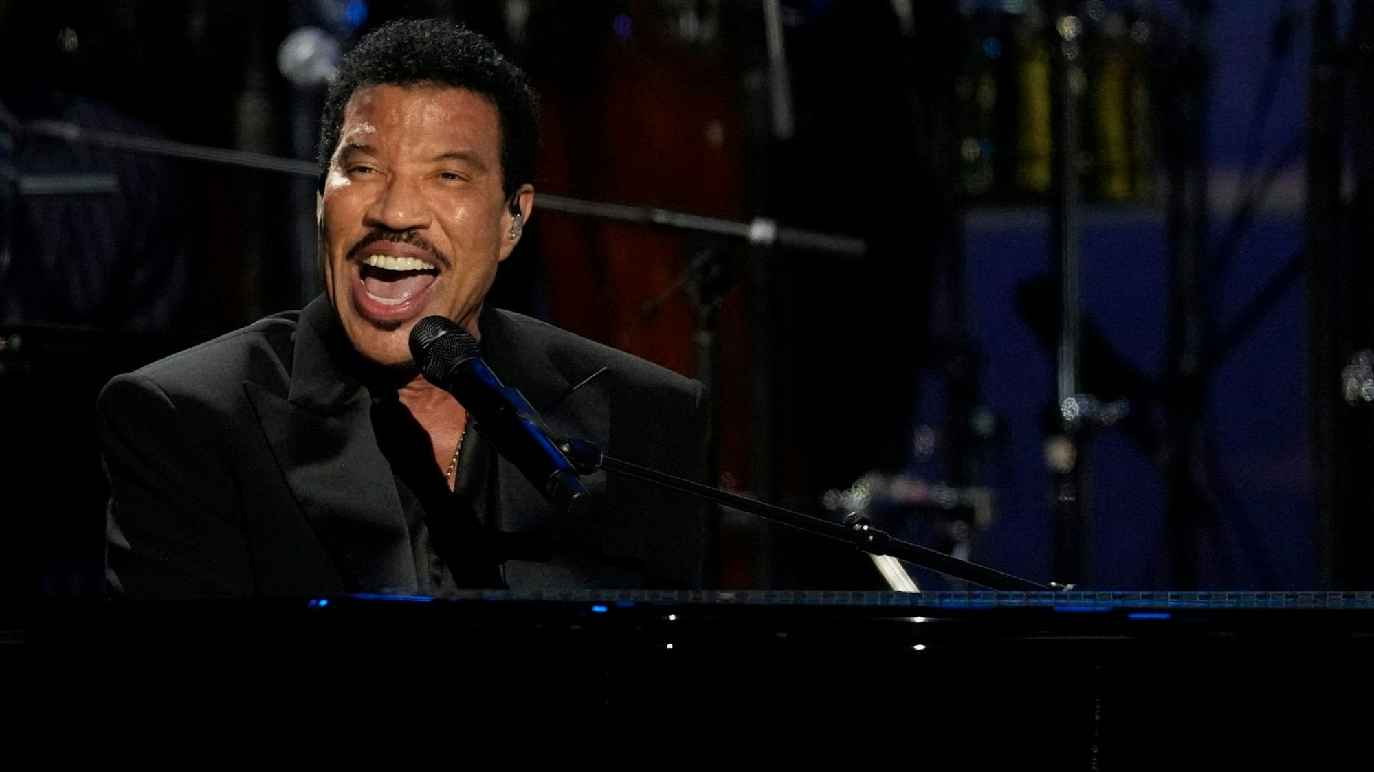 Lionel Richie sitzt an einem Flügel und singt ins Mikrofon.