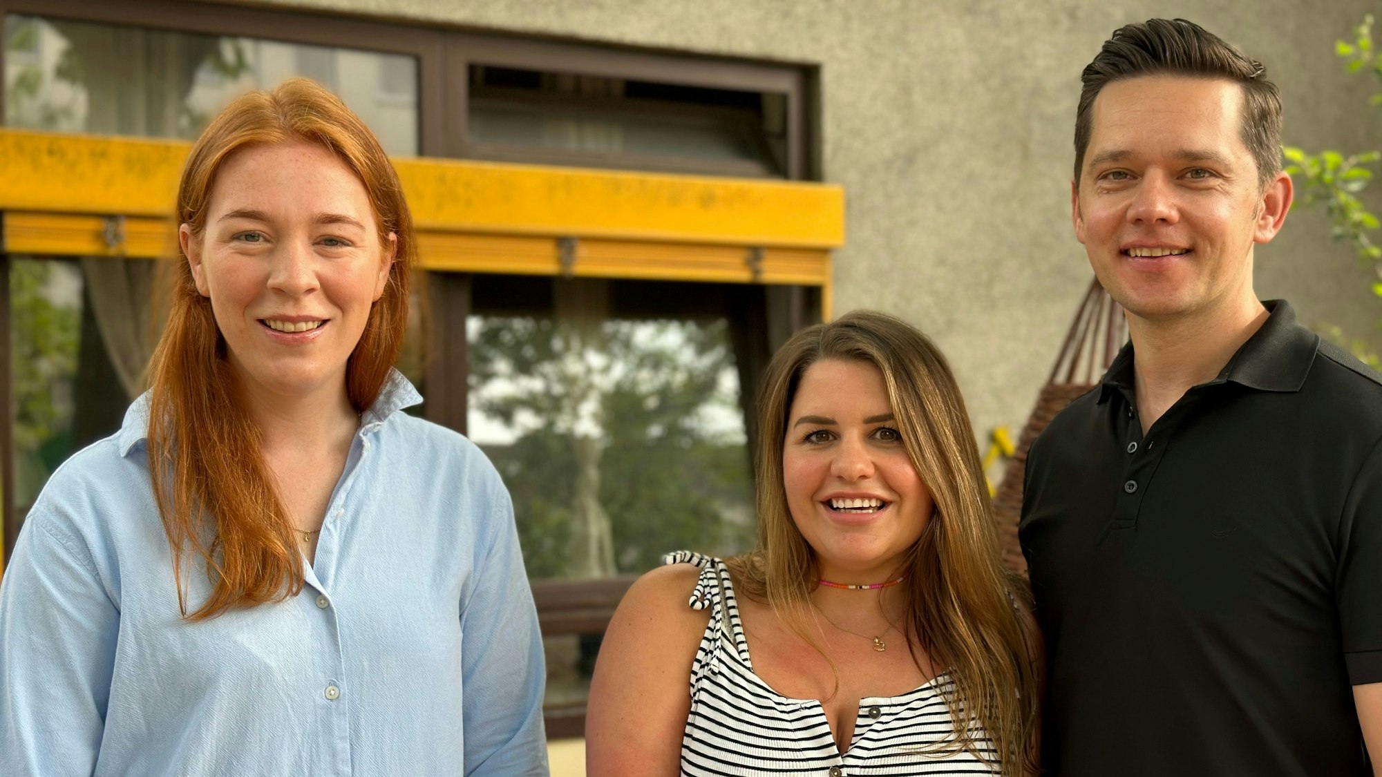 Zwei Frauen und ein Mann stehen vor dem Fenster eines Gebäudes.