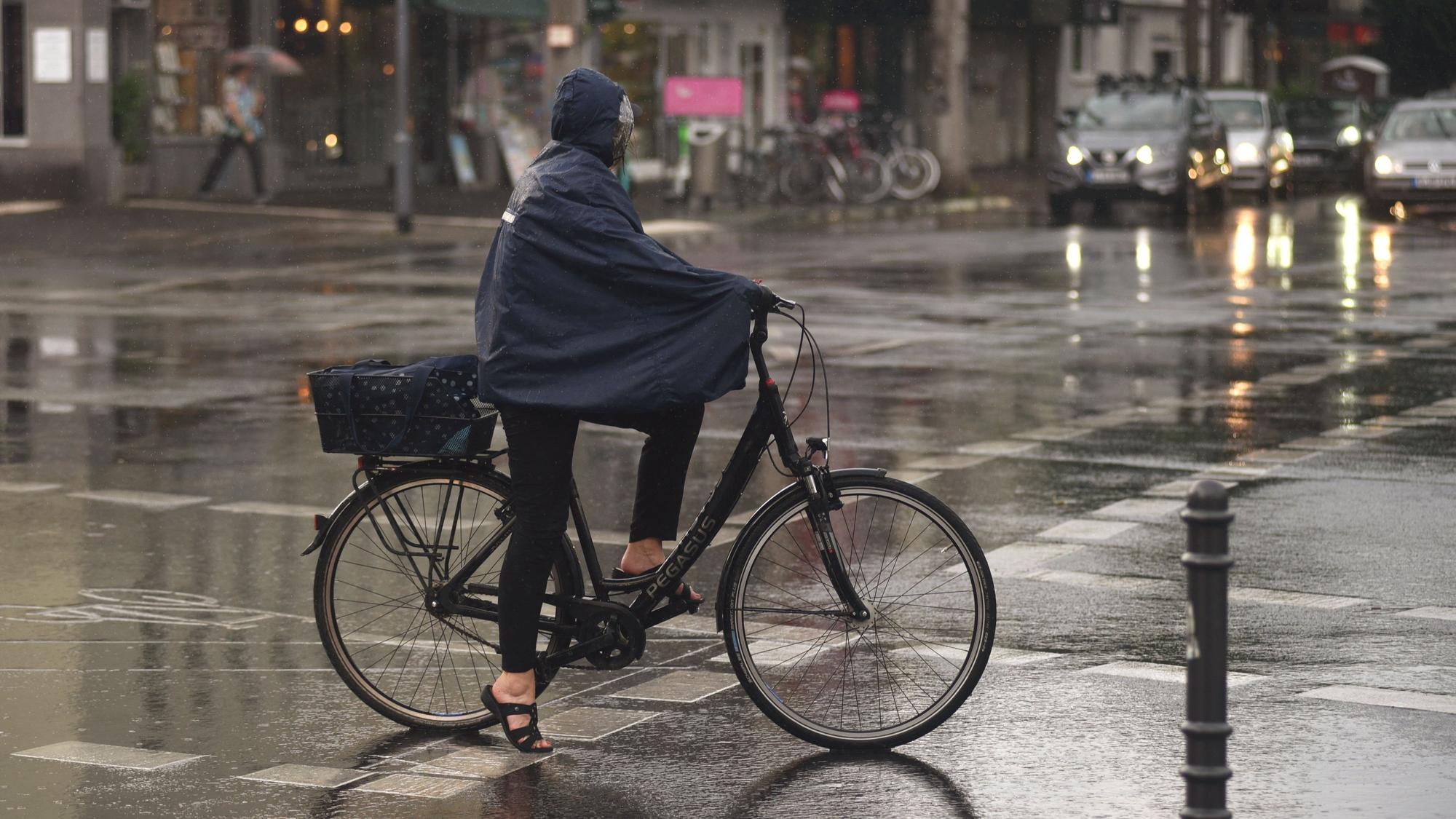 Eine Frau fährt im Regencape mit dem Fahrrad durch den Regen.
