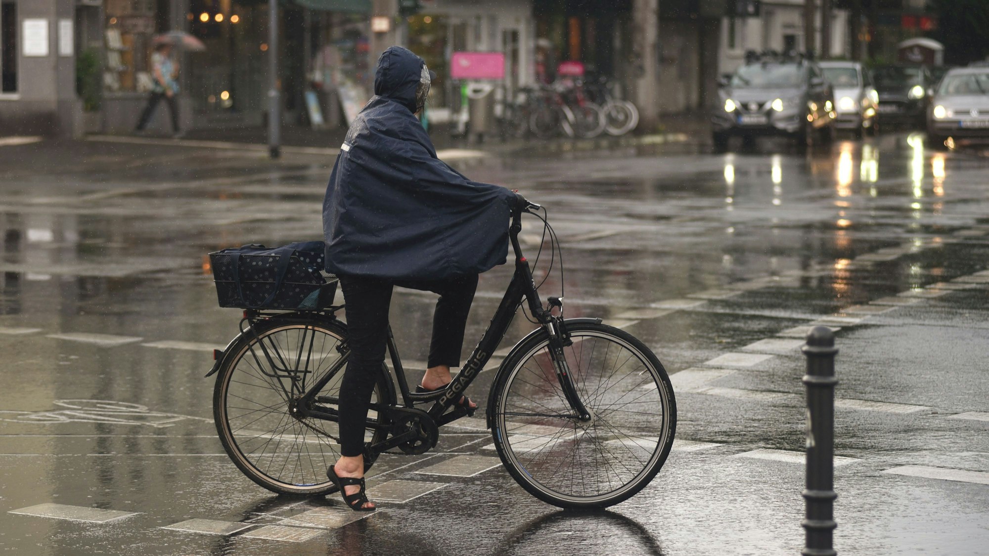 Eine Frau fährt im Regencape mit dem Fahrrad durch den Regen.