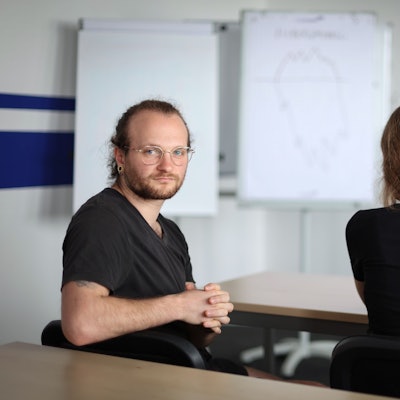 Luca Gagliano schaut ernst in die Kamera. Eine Kommilitonin sitzt mit dem Rücken zur Kamera neben ihm.