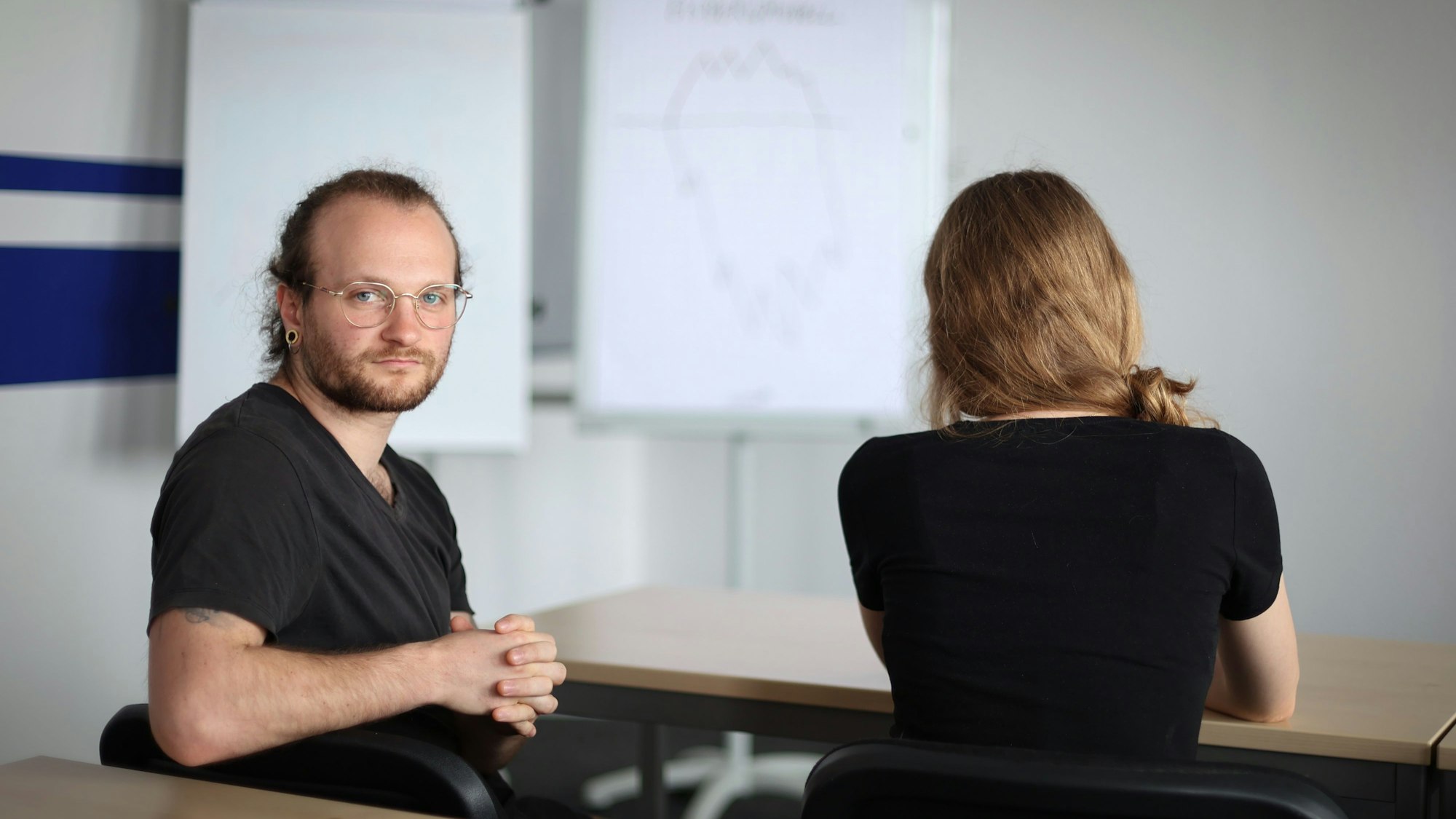 Luca Gagliano schaut ernst in die Kamera. Eine Kommilitonin sitzt mit dem Rücken zur Kamera neben ihm.