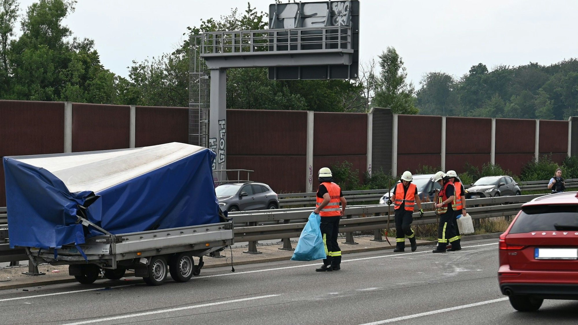 Das Bild zeigt einen Autoanhänger an der Mittelleitplanke und mehrere Feuerwehrleute.