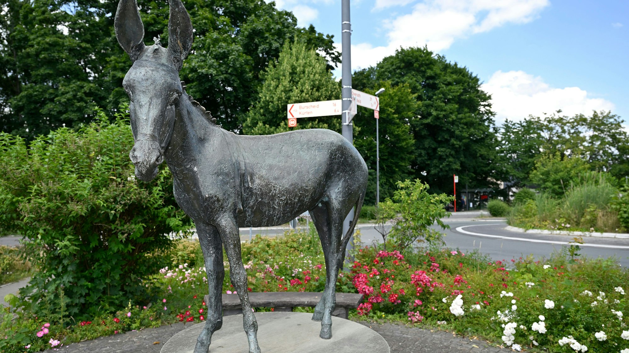 Die Skulptur des Bechener Esels steht vor Blumen.