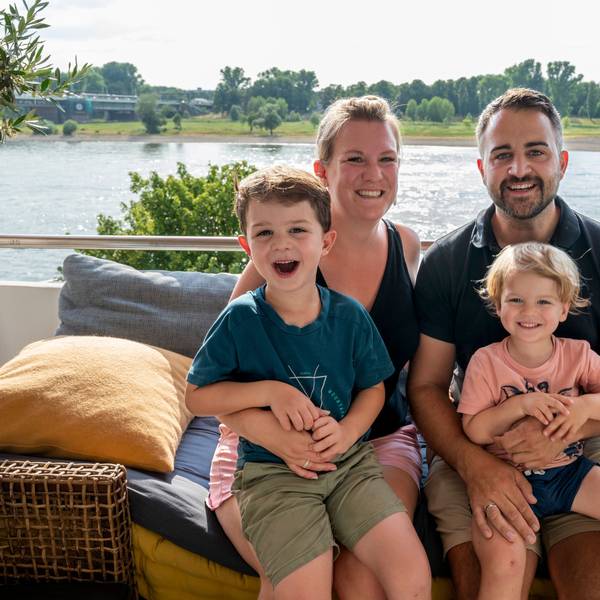 Verena und Caroll Zosel mit Milo (links) und Jarno sitzen auf ihrem Balkon in Mülheim. Im Hintergrund ist der Rhein zu sehen.