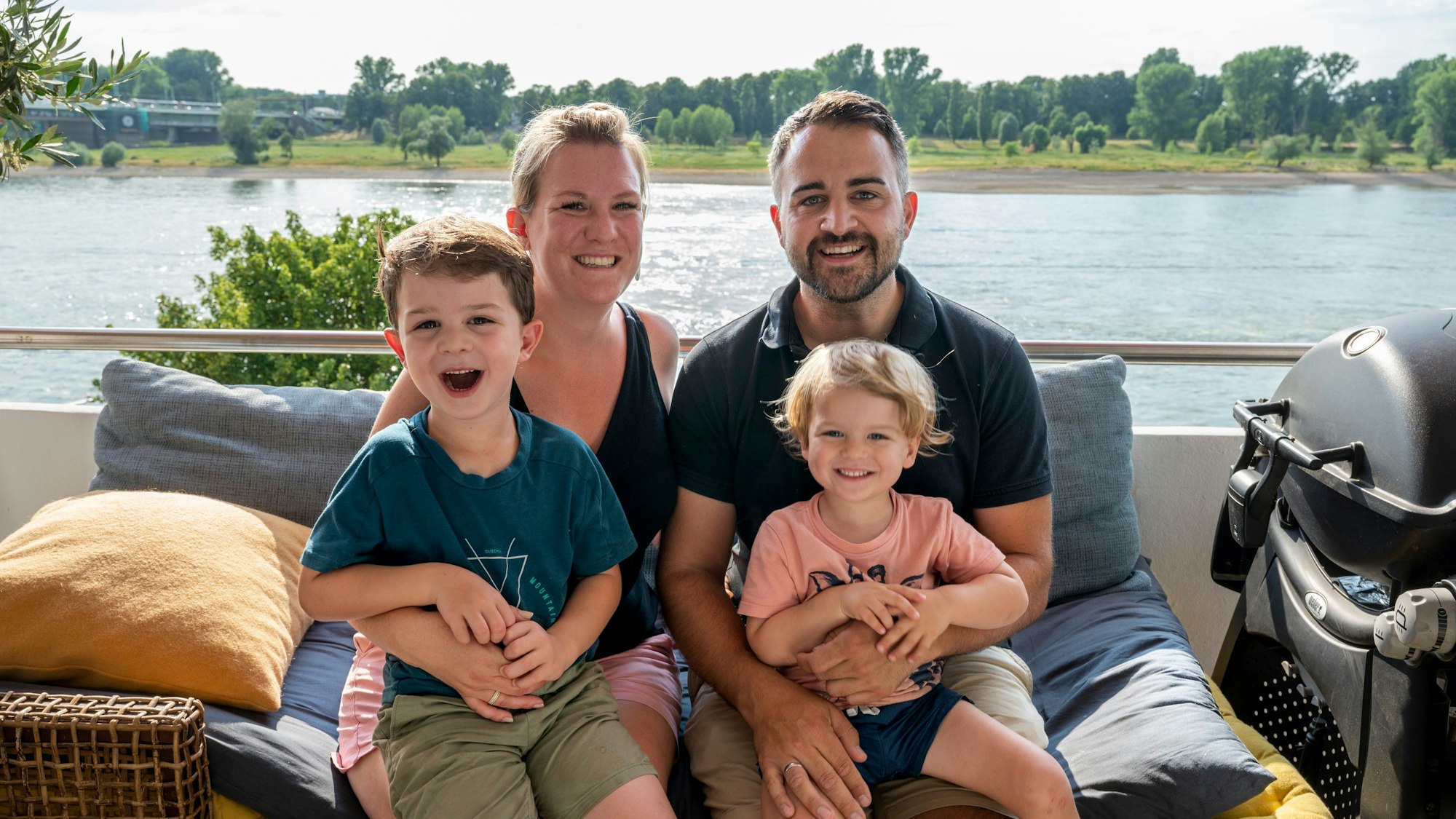Verena und Caroll Zosel mit Milo (links) und Jarno sitzen auf ihrem Balkon in Mülheim. Im Hintergrund ist der Rhein zu sehen.