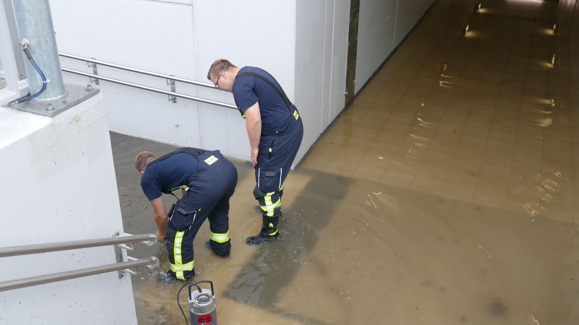 Zwei Feuerwehrleute stehen in der vollgelaufenen Unterführung des Bahnhofs in Friedrich-Wilhelms-Hütte.