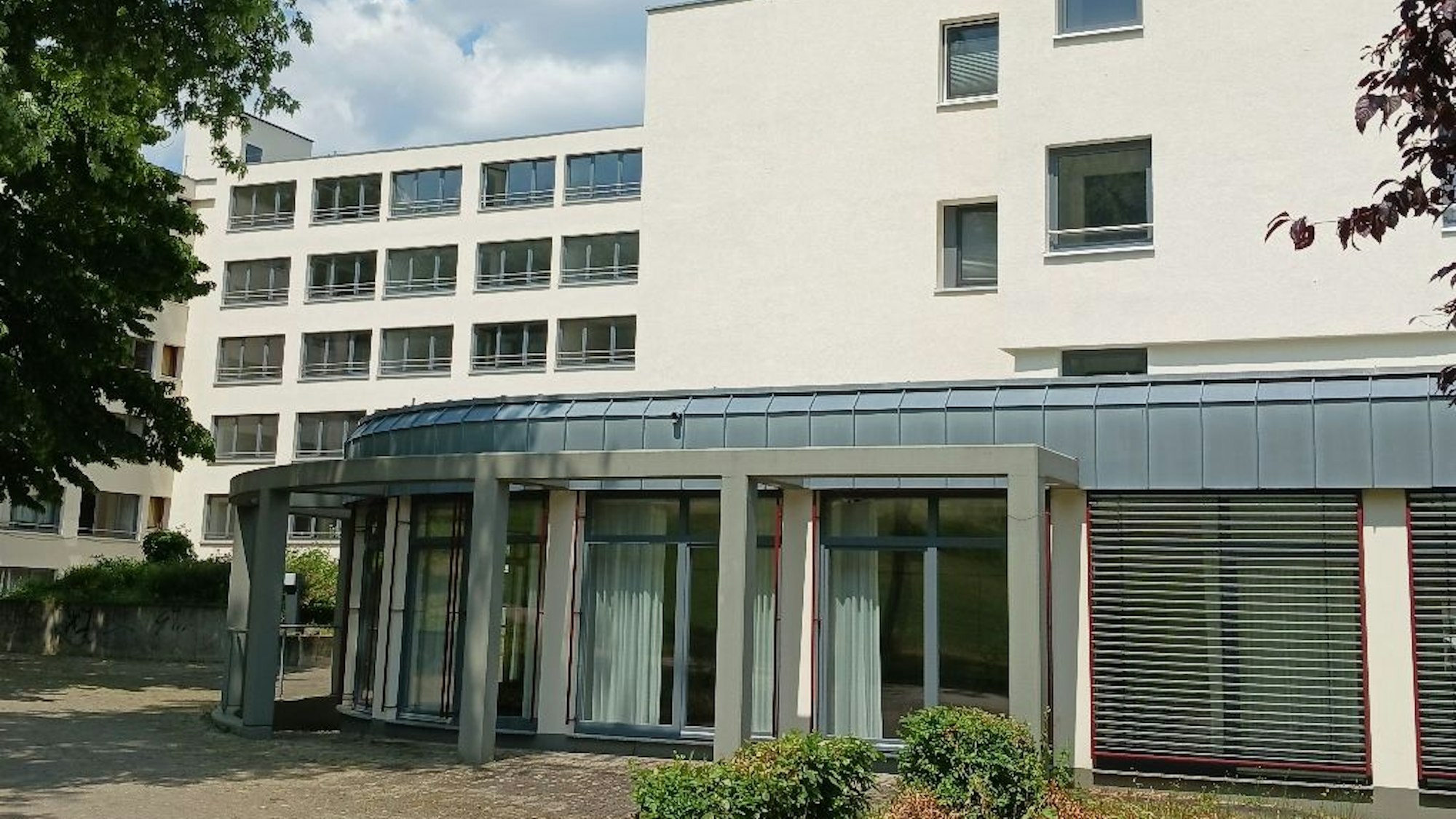 Ein modernes Wohngebäude mit fünf Etagen; im Vordergrund steht ein Anbau mit großen Fenstern.