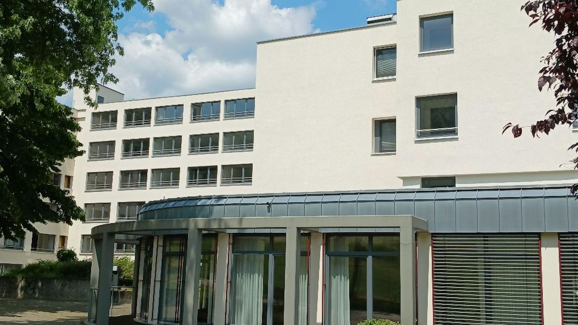 Ein mehrstöckiges weißes Gebäude mit Bäumen, große Terrassentüren und eine Pergola.