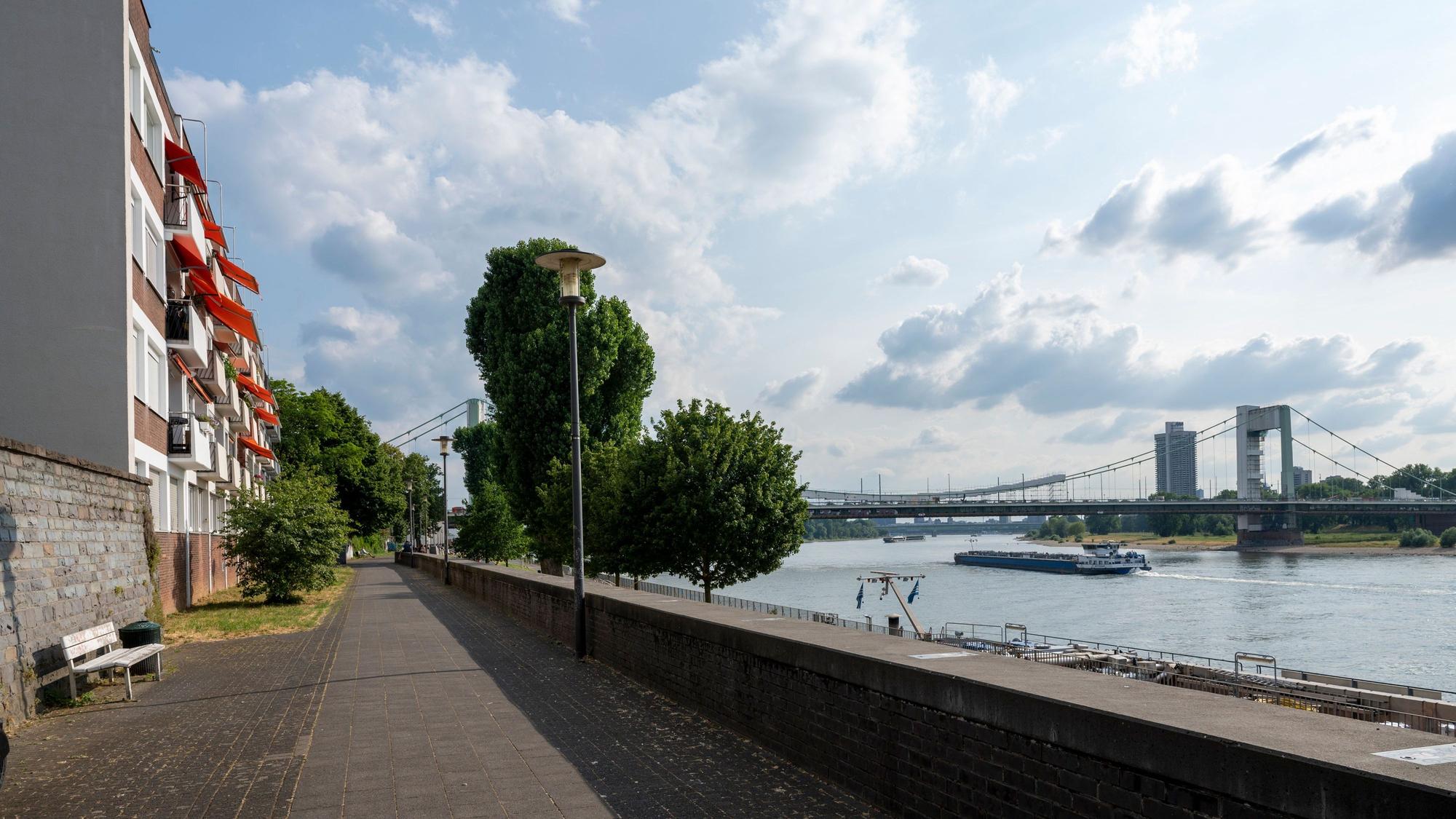 Ein Mehrfamilienhaus mit orangefarbenen Markisen am Mülheimer Rheinufer. Rechts der Rhein und die Mülheimer Brücke