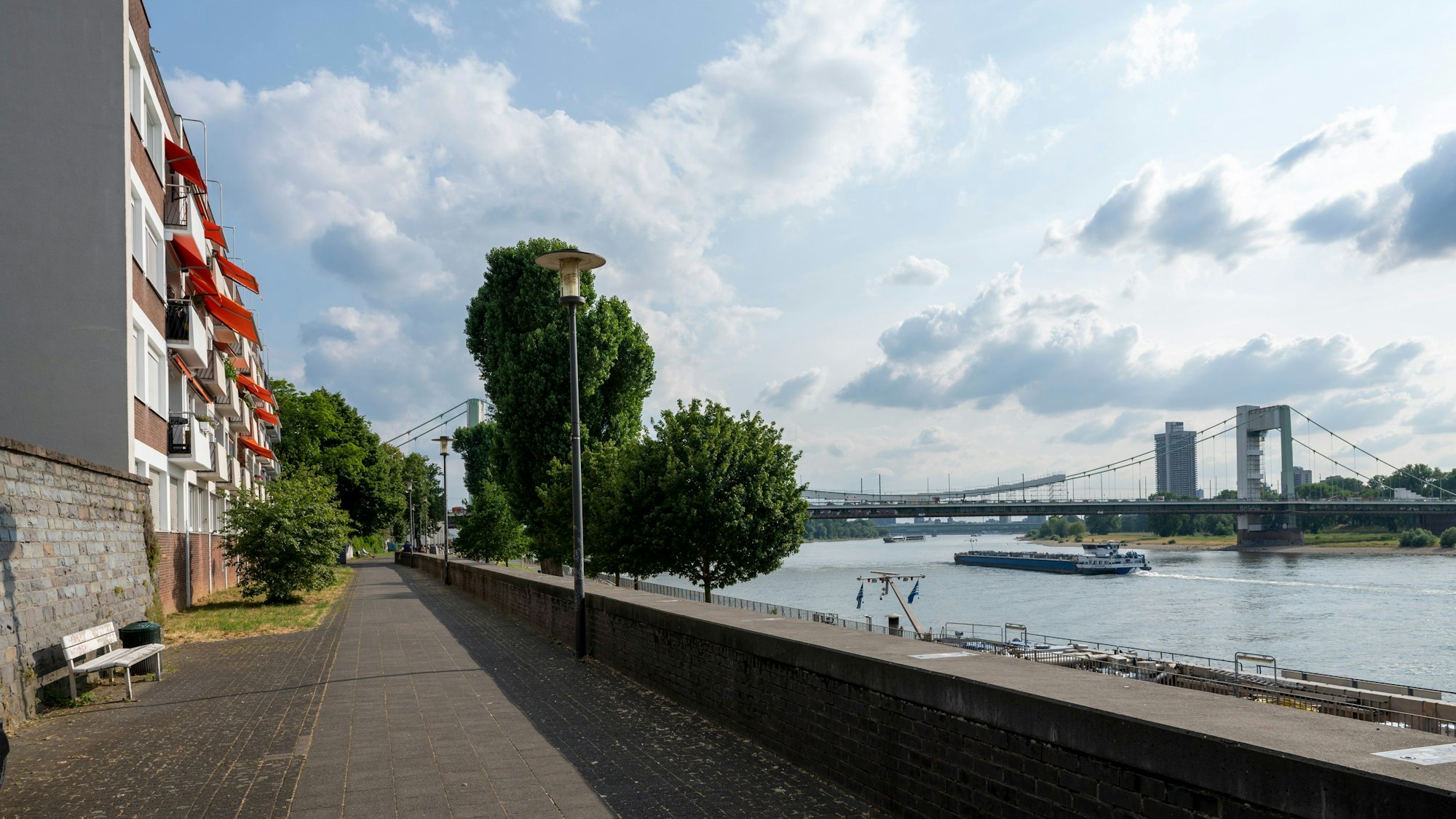 Ein Mehrfamilienhaus mit orangefarbenen Markisen am Mülheimer Rheinufer. Rechts der Rhein und die Mülheimer Brücke