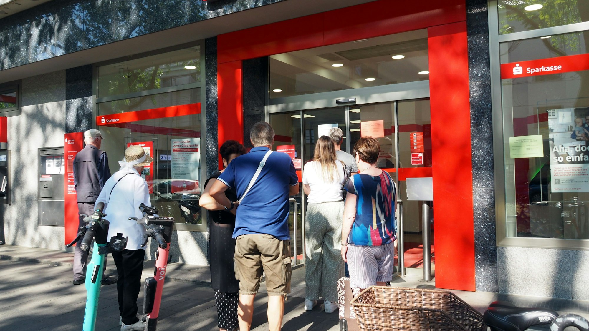 Viele Menschen stehen vor der Sparkasse.