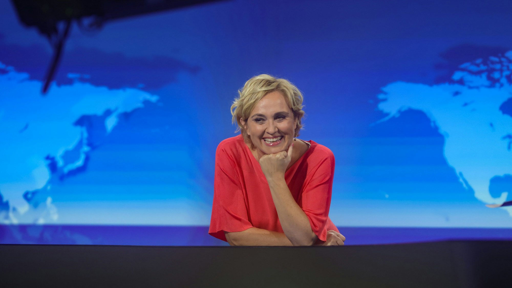 Caren Miosga steht in einem roten Kleid im Studio der „Tagesthemen“ und lacht.
