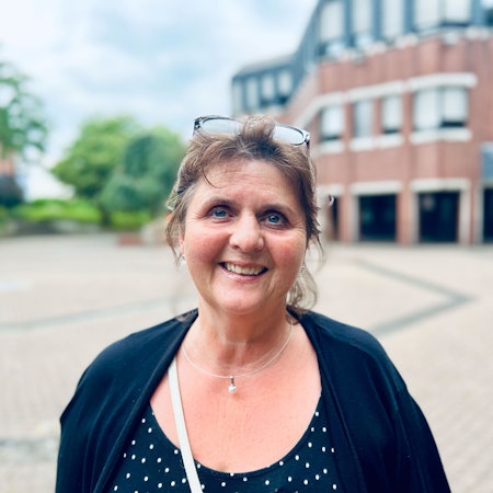 Eine Frau mittleren Alters schaut lächelnd in die Kamera. Die Brille hat sie in ihr dunkles zurückgestecktes Haar hochgeschoben.