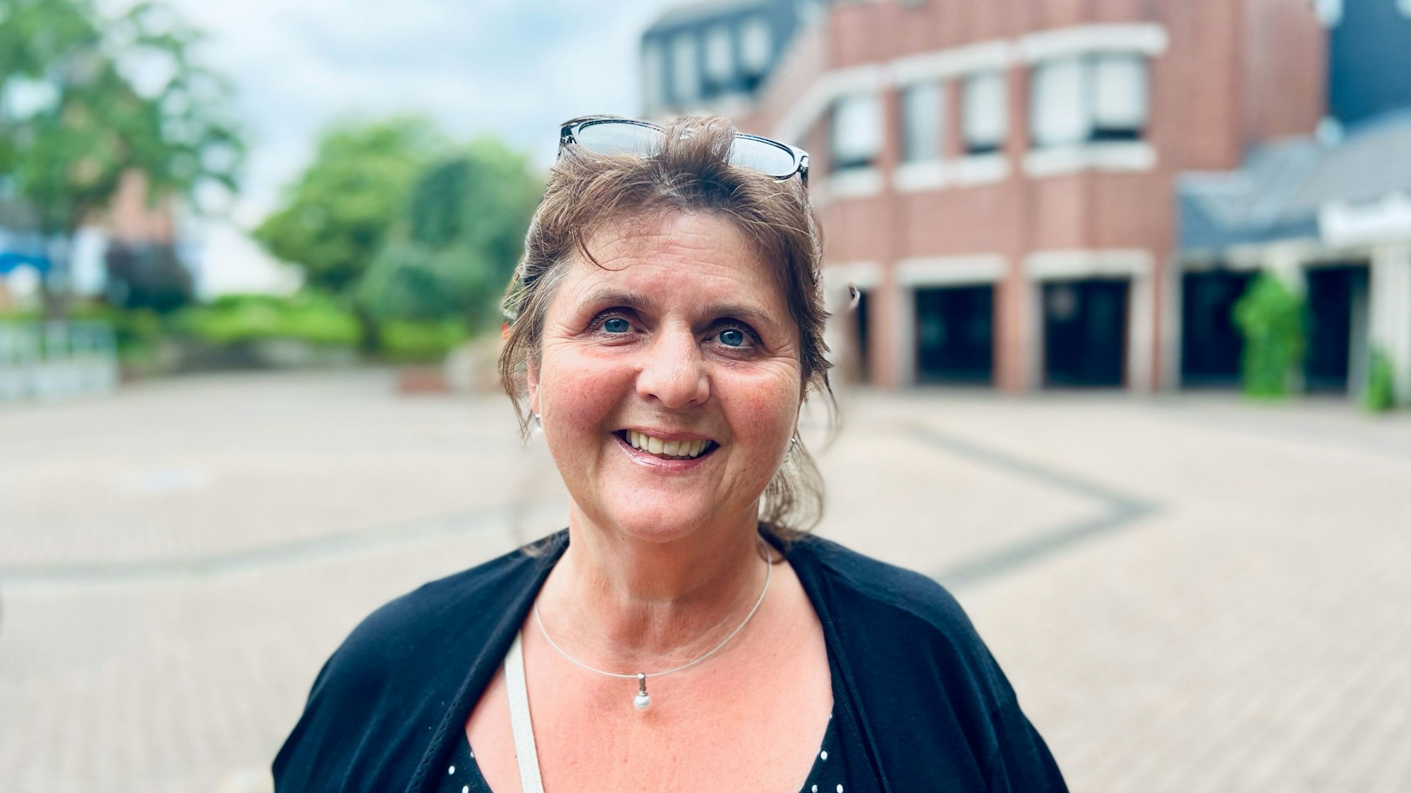 Eine Frau mittleren Alters schaut lächelnd in die Kamera. Die Brille hat sie in ihr dunkles zurückgestecktes Haar hochgeschoben.