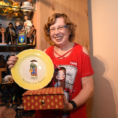 Eine Frau hält eine bunte Stoffkiste und einen Porzellanteller in einer Hand.