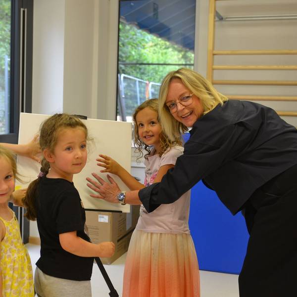 Kindergartenkinder und Bürgermeisterin drücken ihre Hände auf eine Leinwand im Kindergarten.