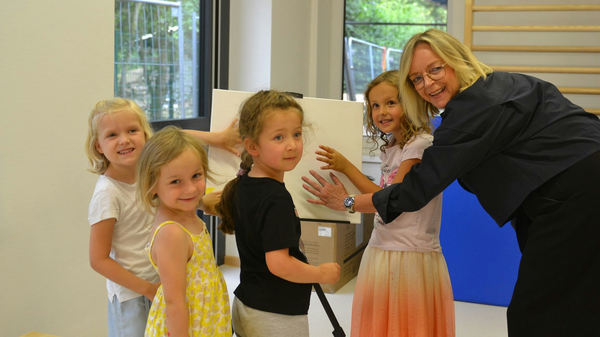 Kindergartenkinder und Bürgermeisterin drücken ihre Hände auf eine Leinwand im Kindergarten.