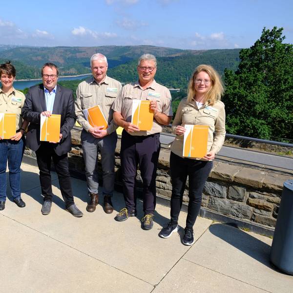 Mehrere Personen in Outdoorkleidung und ein Mann im Anzug präsentieren den Jahresbericht des Nationalparks Eifel.