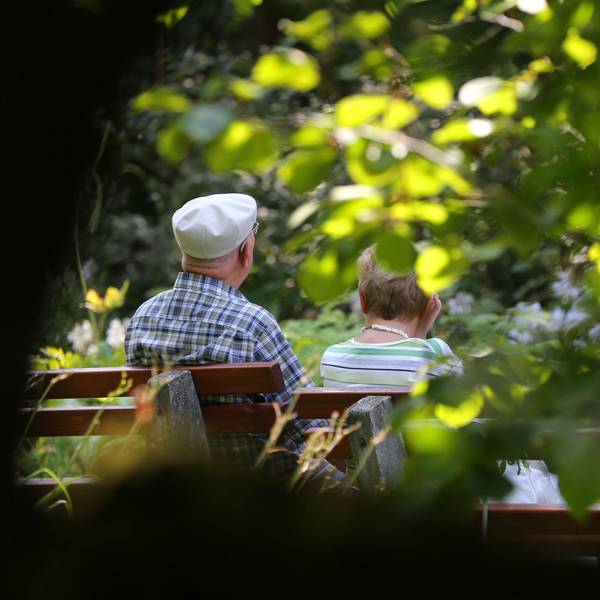 Ein älteres Paar sitzt im Kurpark auf einer Bank im Sonnenschein.