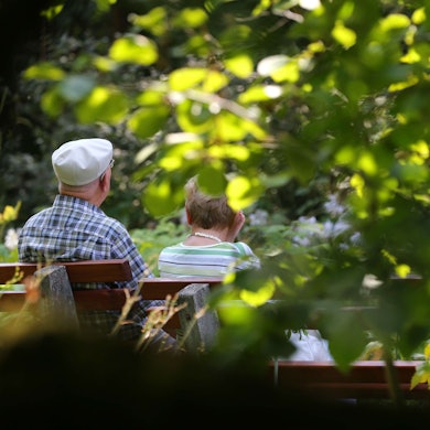 Ein älteres Paar sitzt im Kurpark auf einer Bank im Sonnenschein.