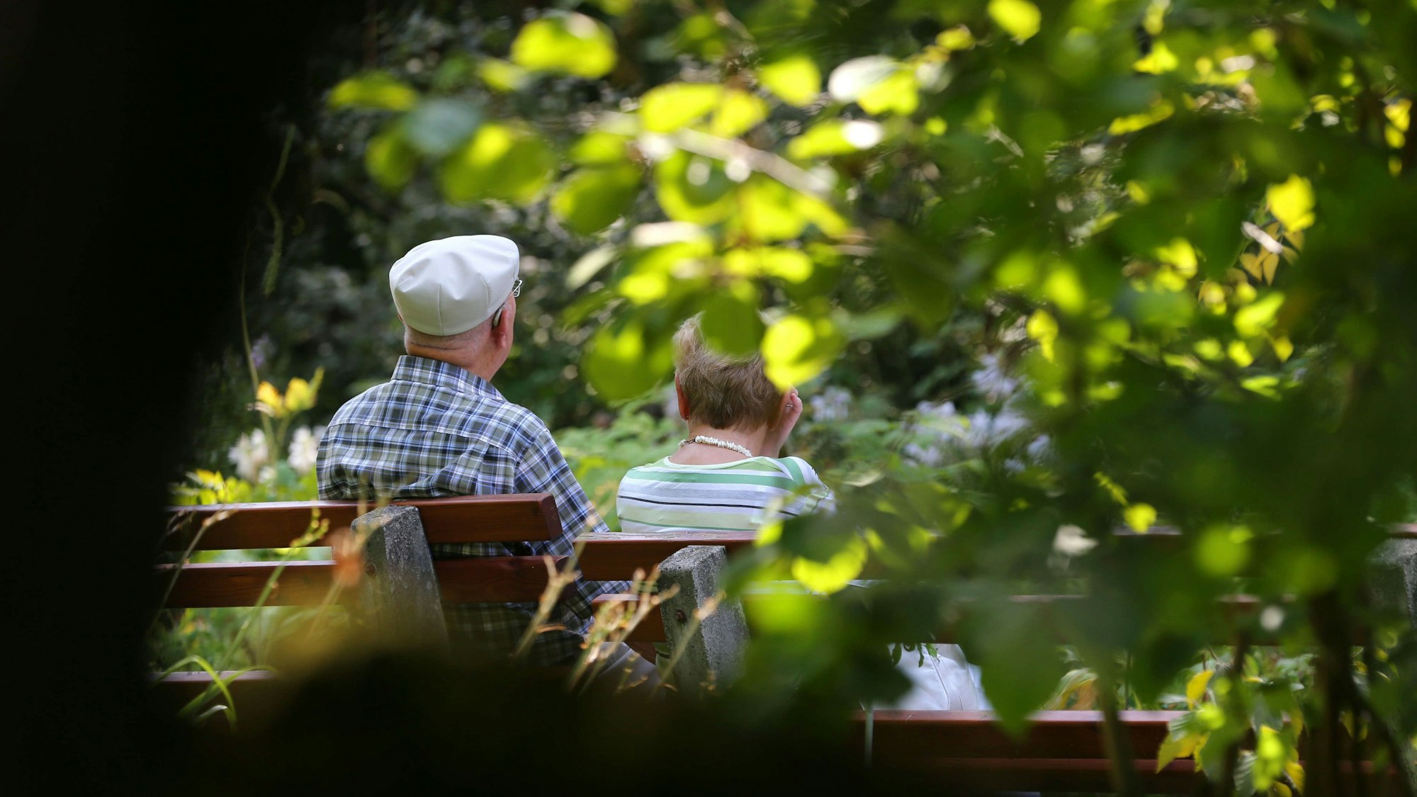 Ein älteres Paar sitzt im Kurpark auf einer Bank im Sonnenschein.