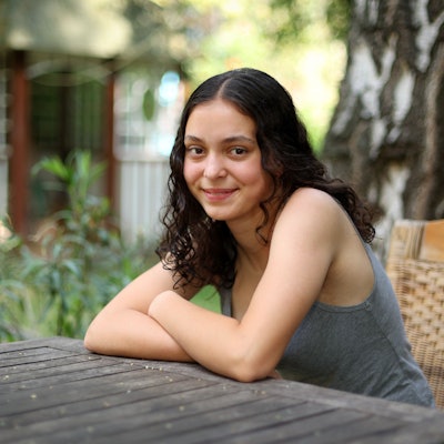 Marlene Skupch (16) aus Neu-Ehrenfeld sitzt in einem Sommergarten am Holztisch.