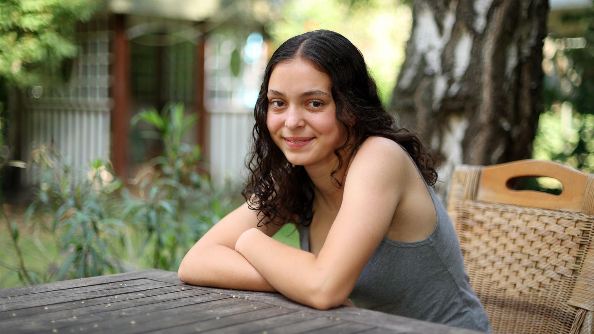 Marlene Skupch (16) aus Neu-Ehrenfeld sitzt in einem Sommergarten am Holztisch.