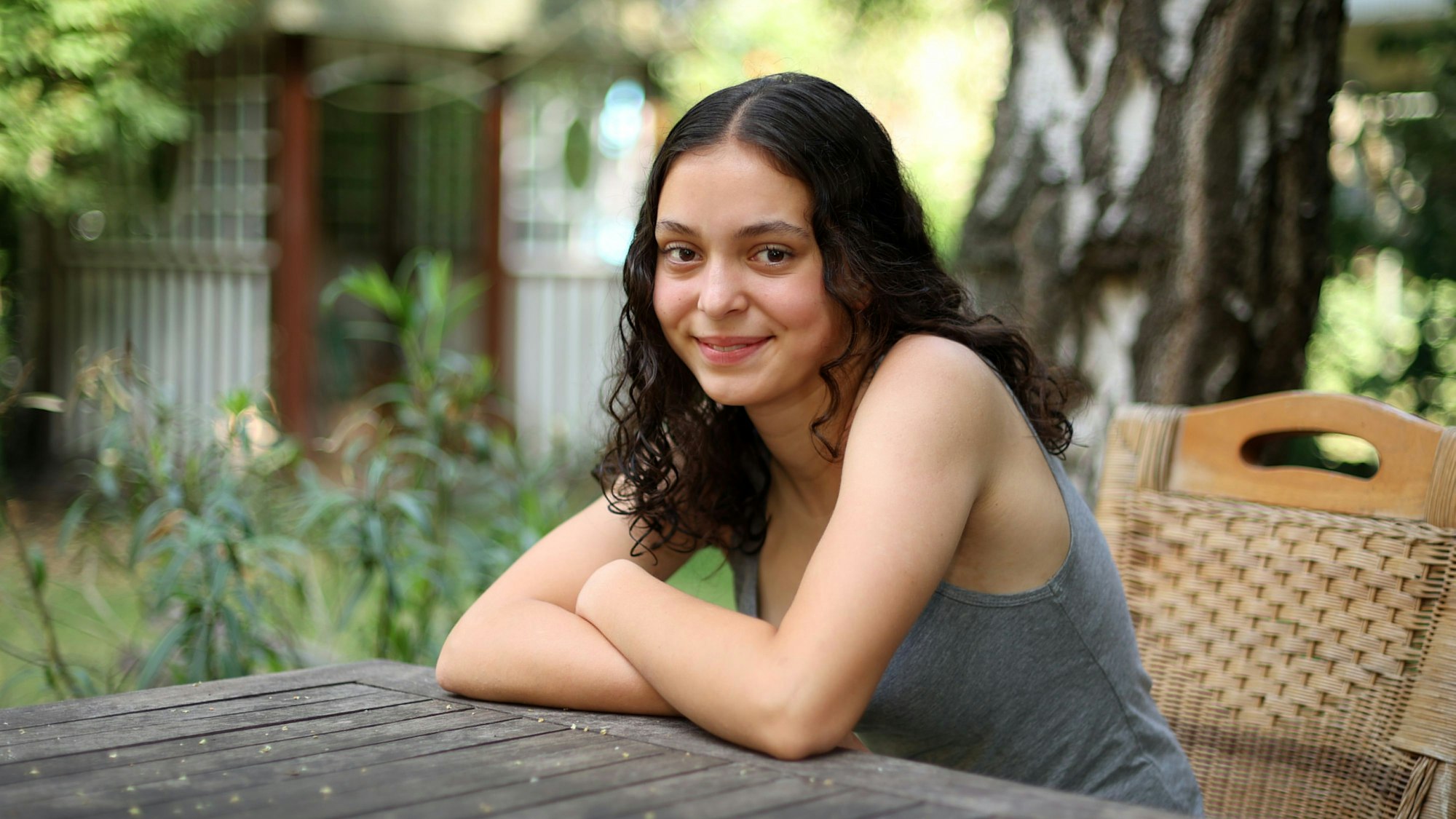 Marlene Skupch (16) aus Neu-Ehrenfeld sitzt in einem Sommergarten am Holztisch.