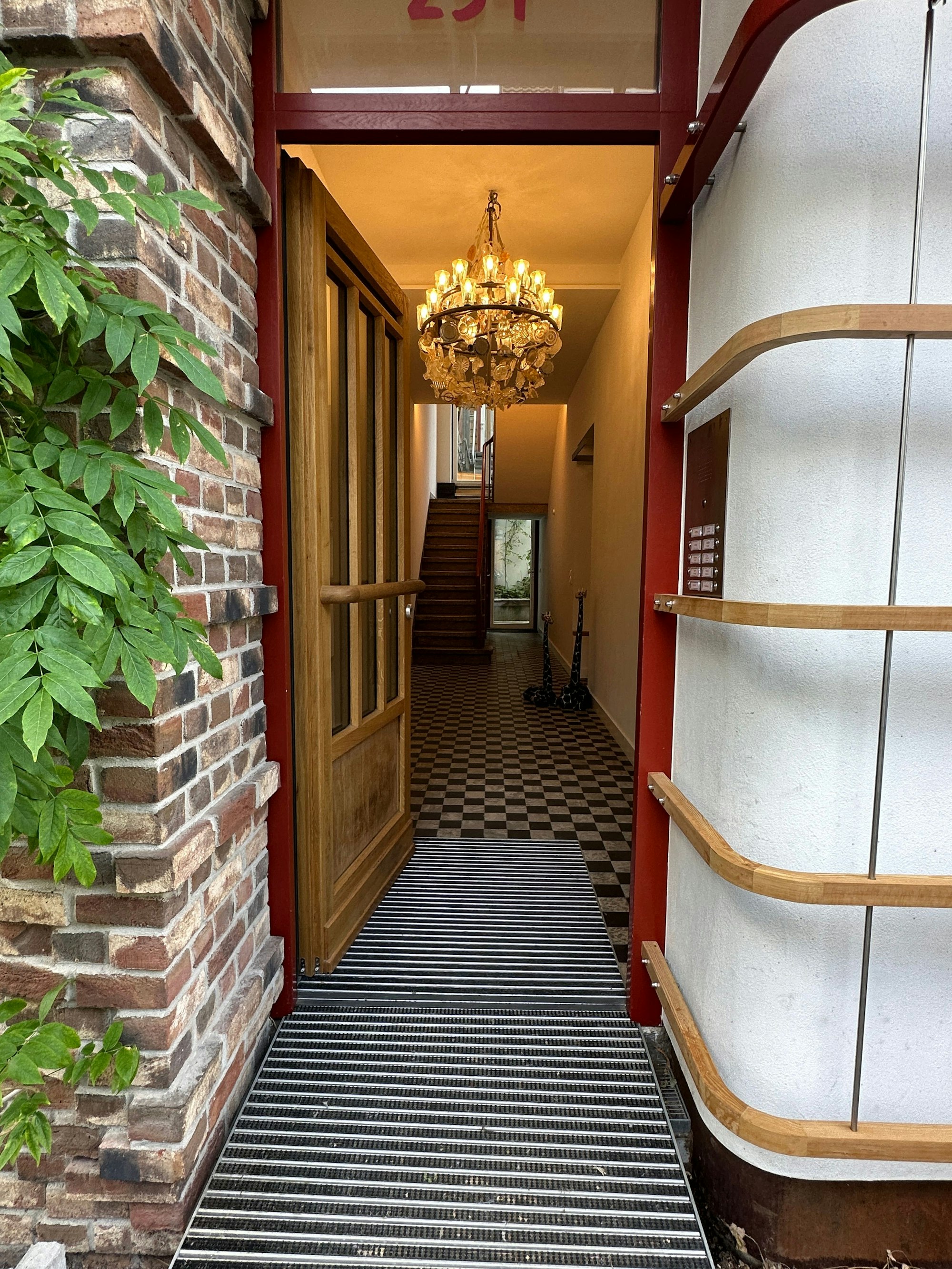 Eine Haustür steht offen, im Flur hängt ein Kronleuchter, der Boden ist klassisch weiß-dunkelbraun gefliest.