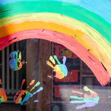 Kinderhände und ein Regenbogen sind an einer Kita zu sehen.