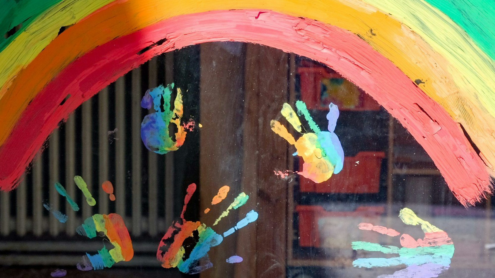Kinderhände und ein Regenbogen sind an einer Kita zu sehen.