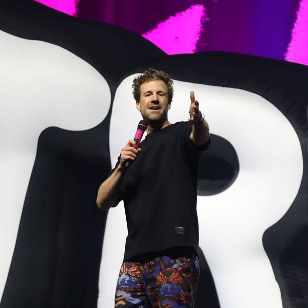Luke Mockridge steht in einem schwarzen T-Shirt, einer bunten Hose und mit einem pinken Mikrofon in der Kölner Lanxess-Arena auf der Bühne.