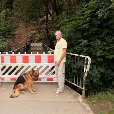 Ein Mann und ein Hund stehen vor dem gesperrten Zugang zu einer Brücke.