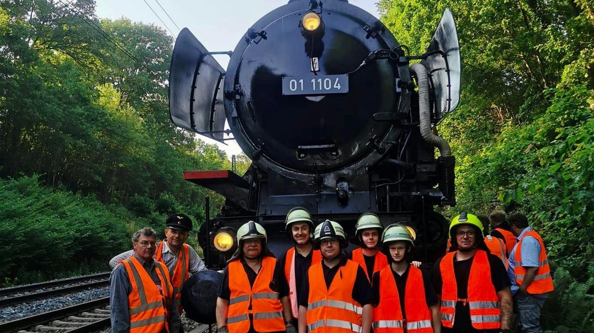 Die Leichlinger Feuerwehrleute vom Löschzug 1 stehen vor der Dampflok 01 1104 auf den Gleisen.