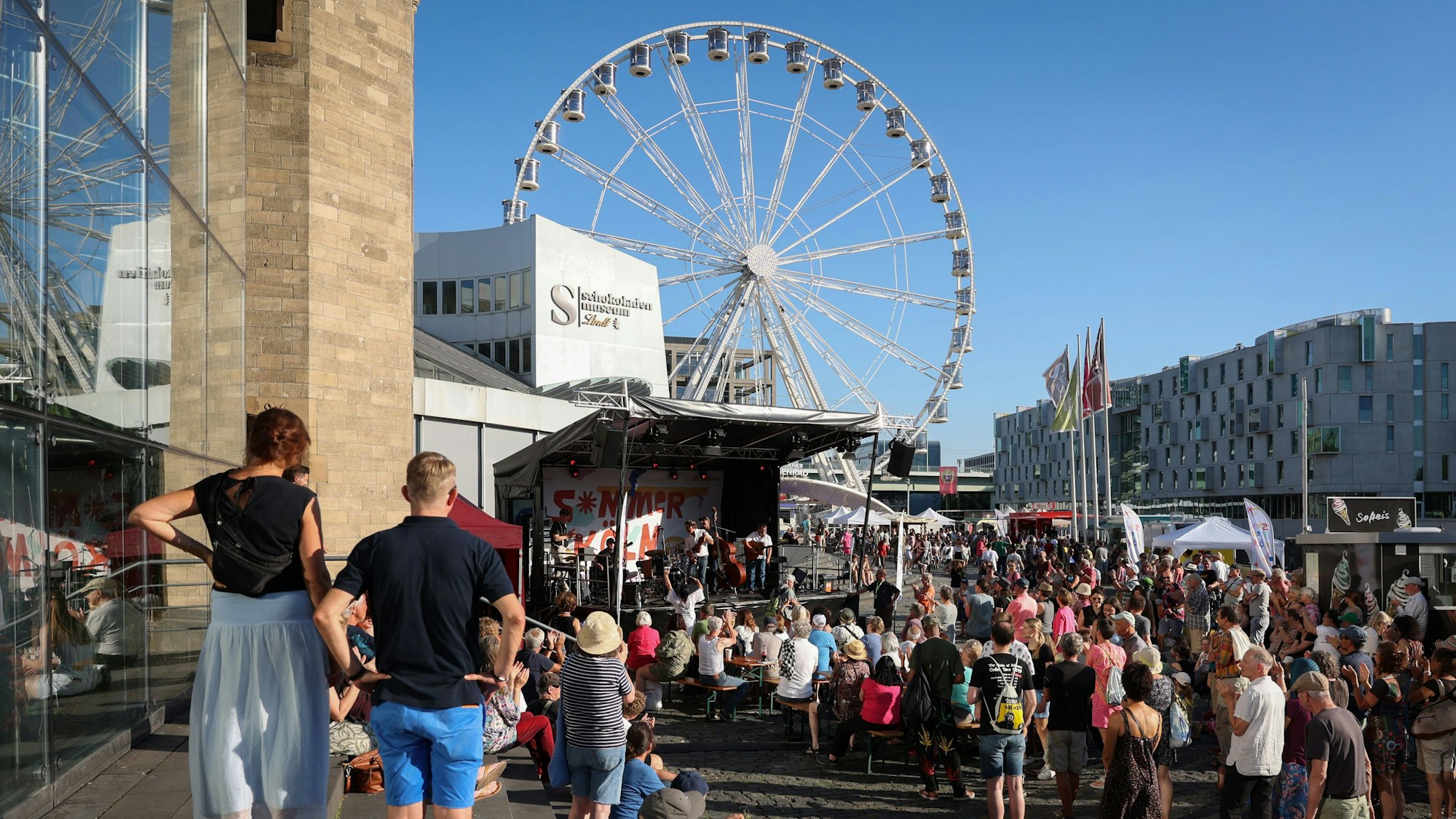 Eine Bühne ist vor dem Schokoladenmuseum aufgebaut, davor stehen viele Menschen.