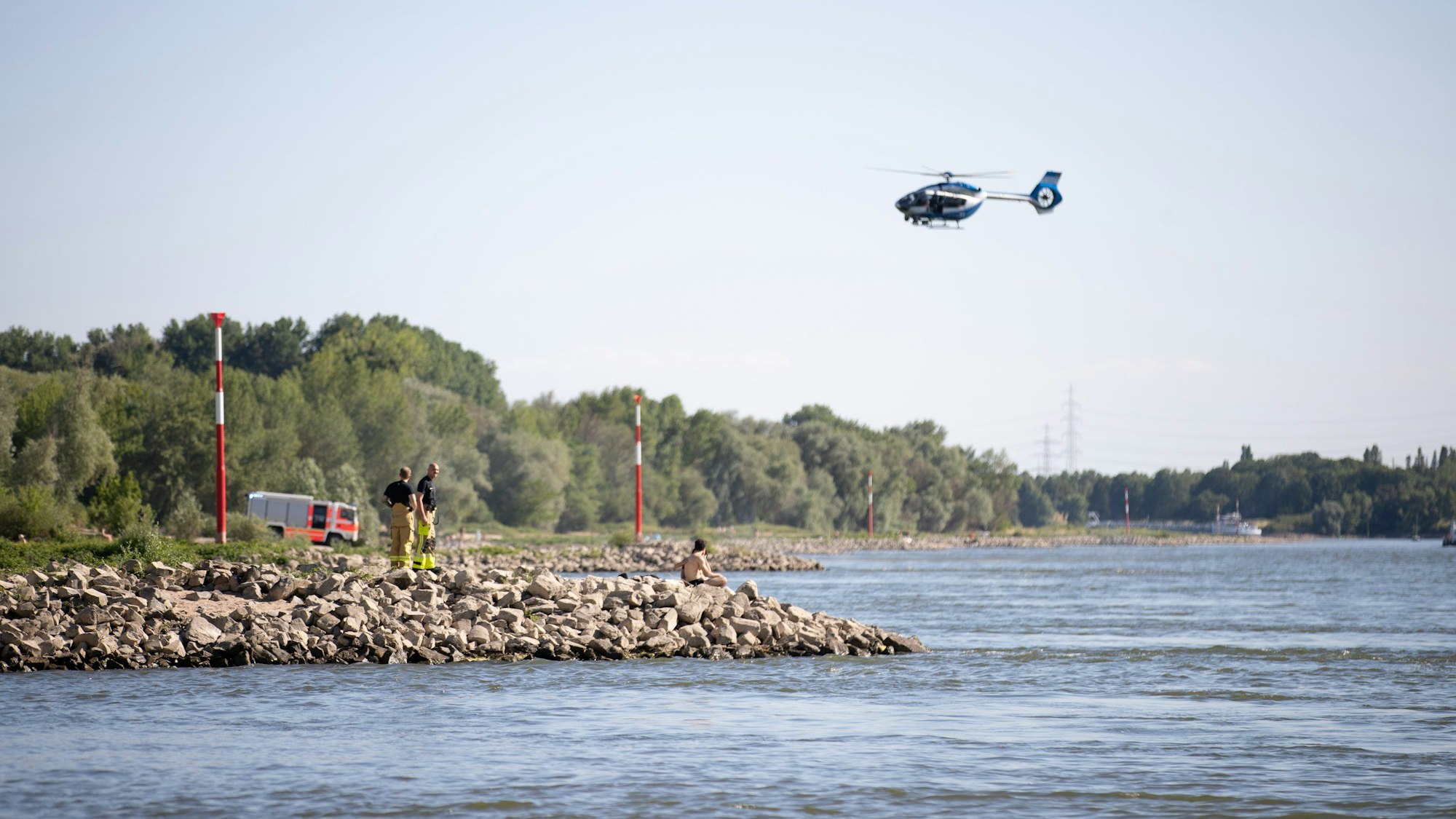 Aus einem Hubschrauber und vom Ufer aus suchen Einsatzkräfte nach einem Schwimmer, der im Rheim von einem Sog erfasst und mitgerissen wurde.