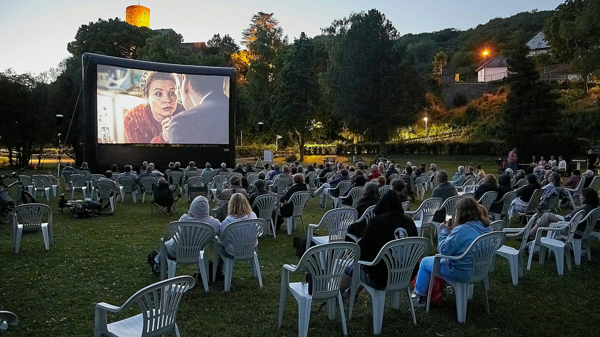 Das Foto zeigt die große Leinwand und das Publikum davor. Im Hintergrund erstrahlt die Heimbacher Burg