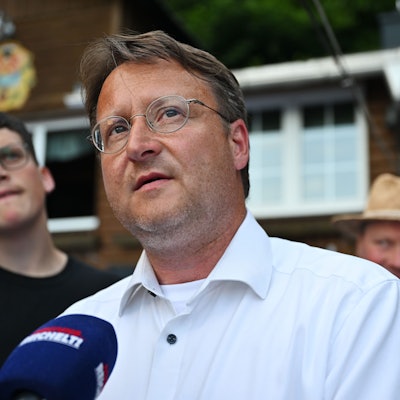 Robert Sesselmann trägt ein weißes Hemd. Er steht vor einem Mikrofon und gibt ein Interview.